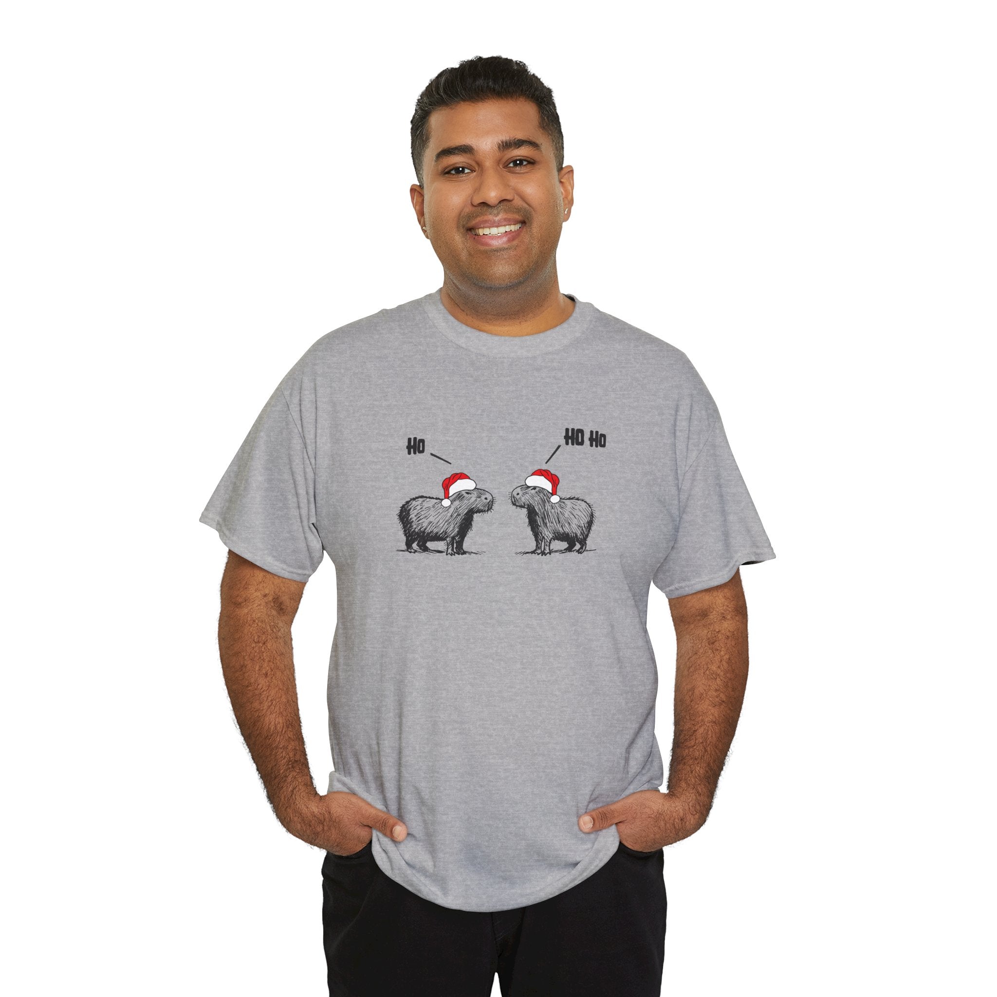 Man wearing a gray short-sleeve crewneck t-shirt featuring a graphic of two fluffy capybara wearing red Santa hats, with 'Ho Ho Ho' text above them,