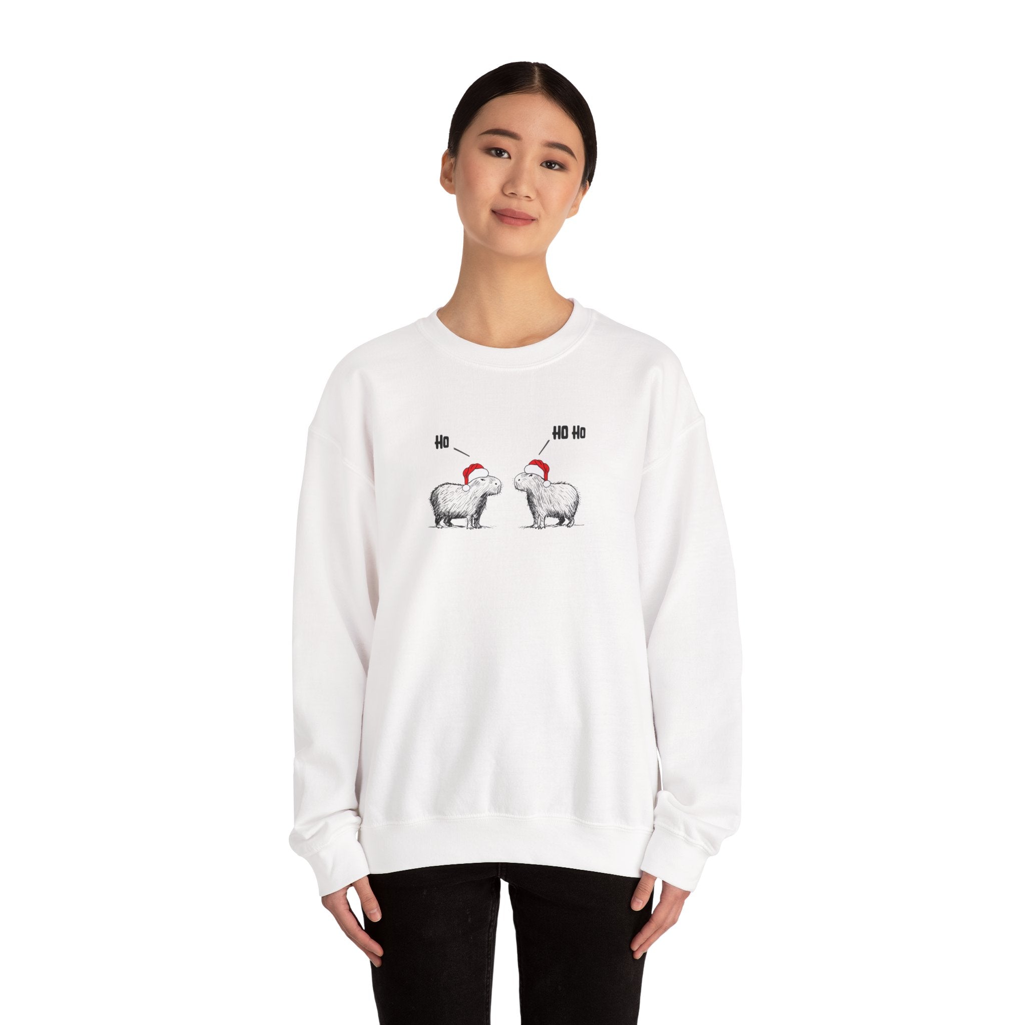 Person wearing a white crewneck sweatshirt featuring a graphic of two capybaras wearing red Santa hats facing each other with 'HO HO HO' text above them