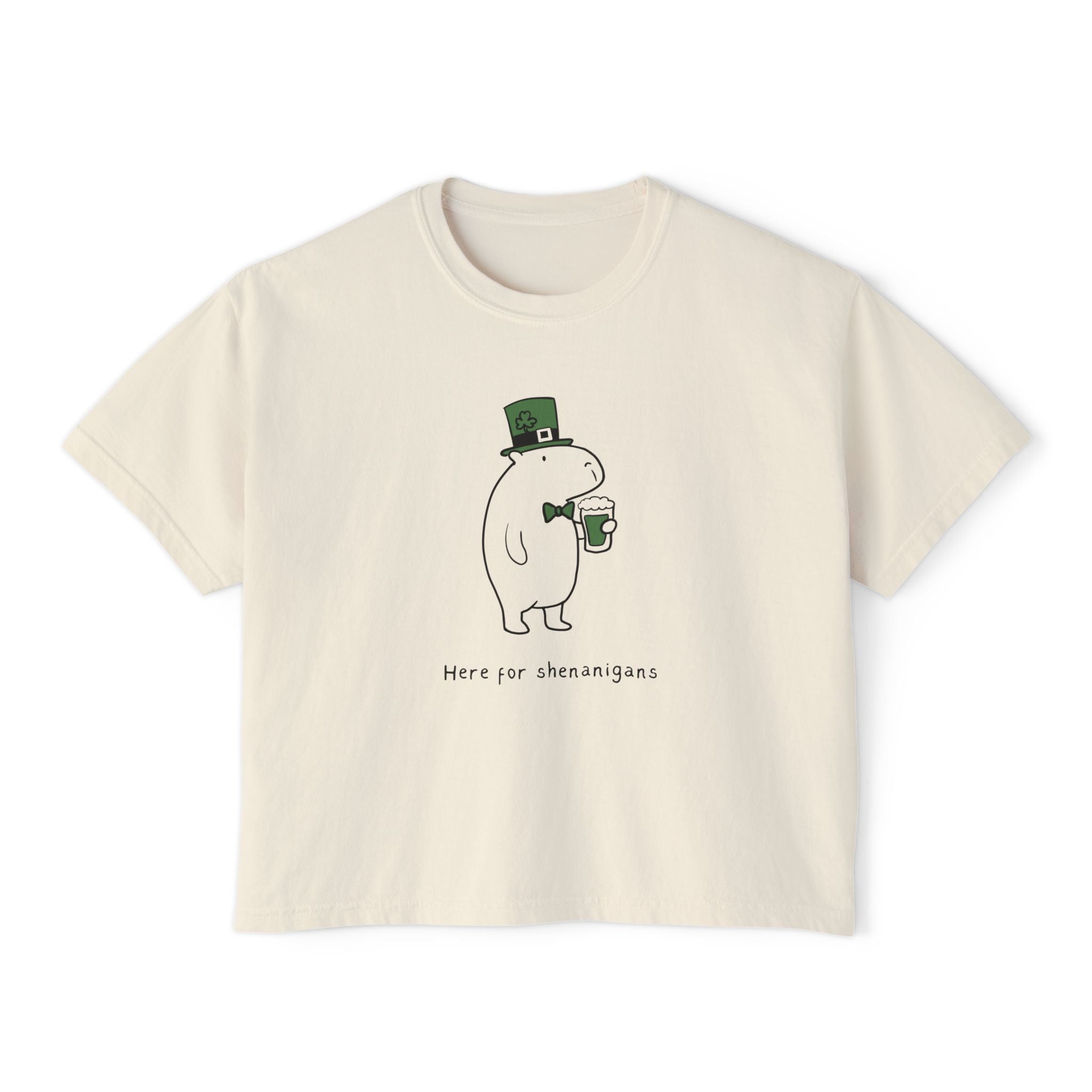 Cream-colored women's boxy t-shirt with a cartoon character holding a green beer mug and wearing a leprechaun hat, text "Here for shenanigans".
