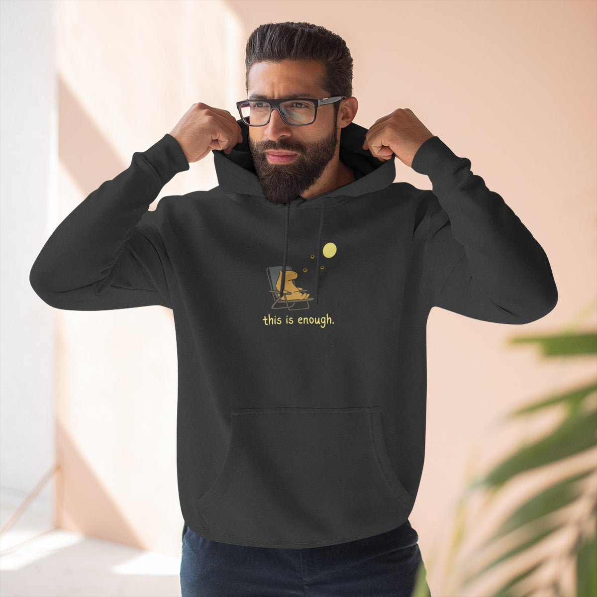 A man wearing a black Capy Life fleece hoodie with a minimalist capybara moonlit graphic and this is enough text.
