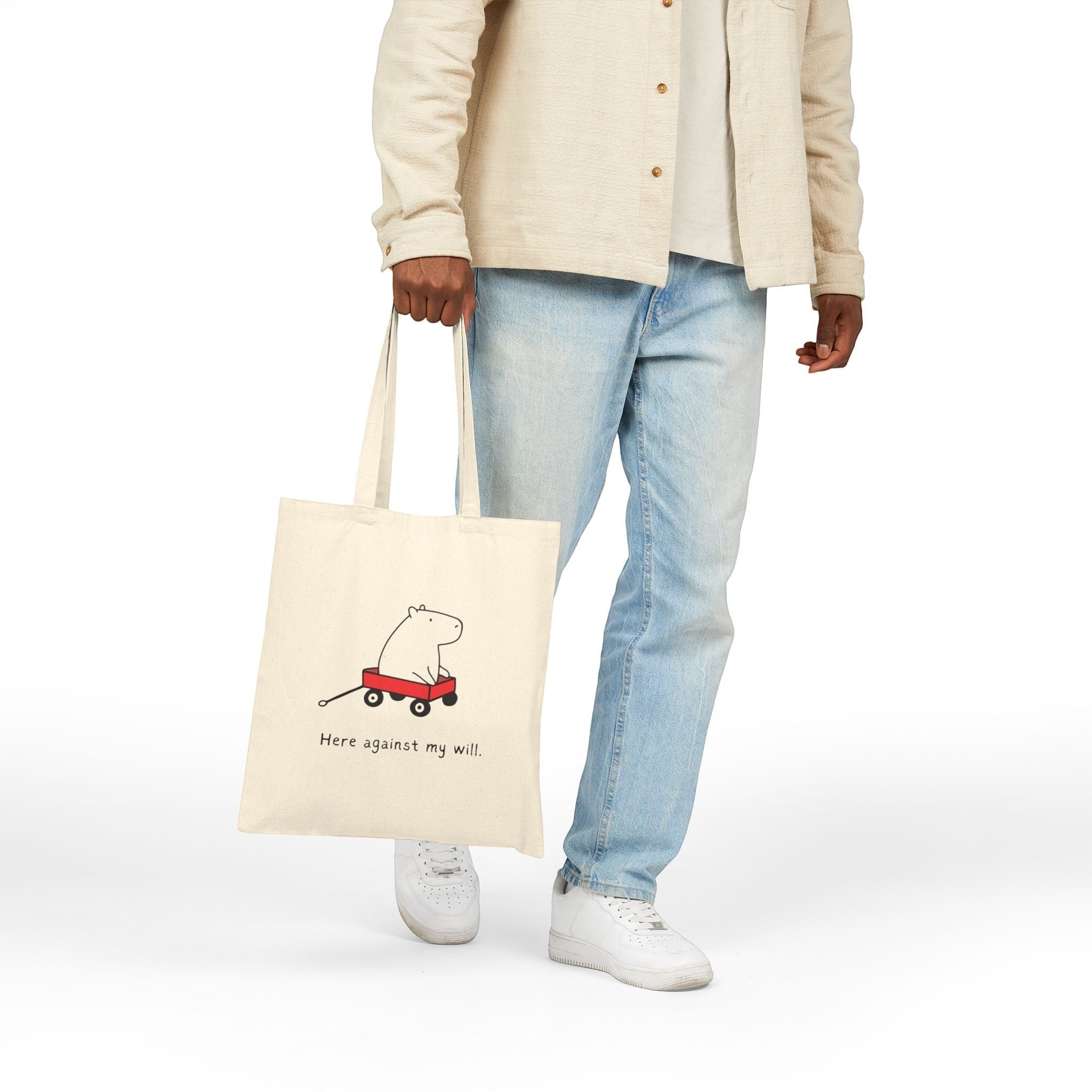 Capy Life natural canvas tote bag featuring a funny capybara in a red wagon with the text Here against my will.