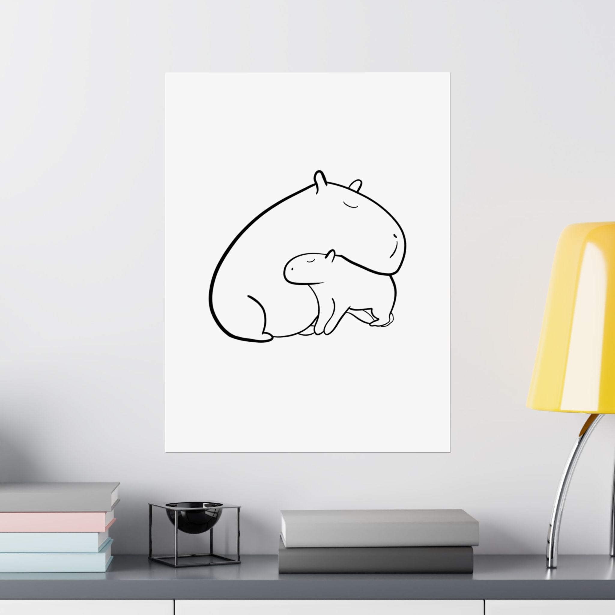 Capy Life minimalist black line drawing of a mama and baby capybara on a white wall above a desk with a yellow lamp.