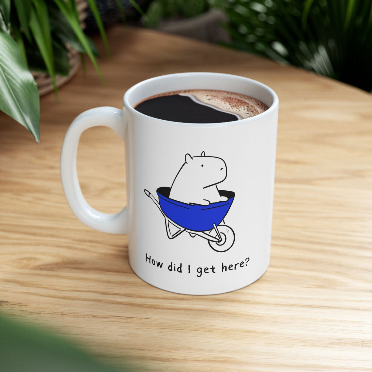 Capy Life white ceramic coffee mug featuring a cute capybara sitting in a blue wheelbarrow with the text How did I get here?