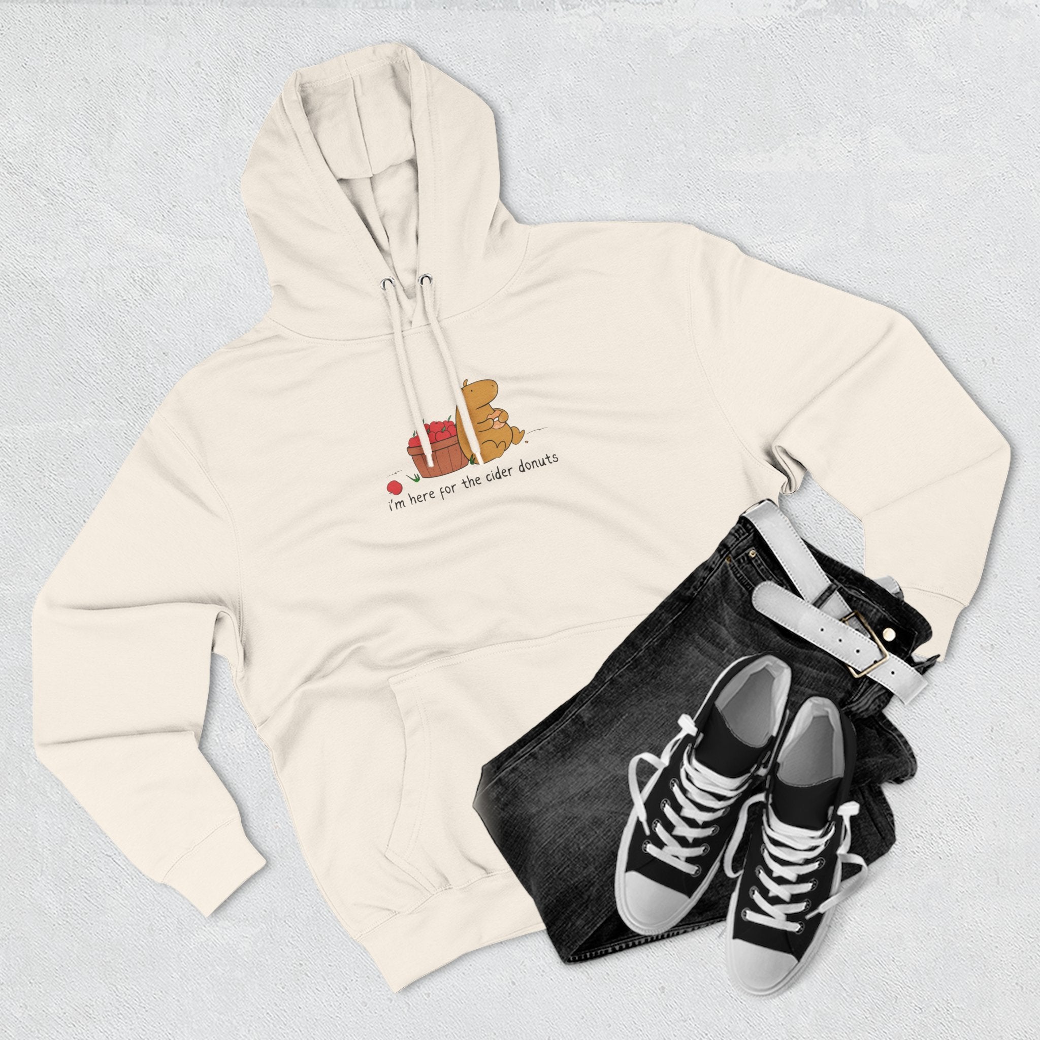 Capy Life cream fleece hoodie featuring a cute capybara eating a donut with apples, styled with black jeans and sneakers.