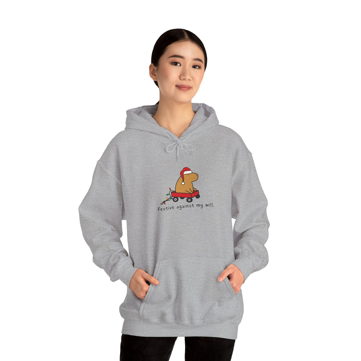 A woman wearing a grey Capy Life hoodie featuring a capybara in a red wagon with a Santa hat and Christmas lights.