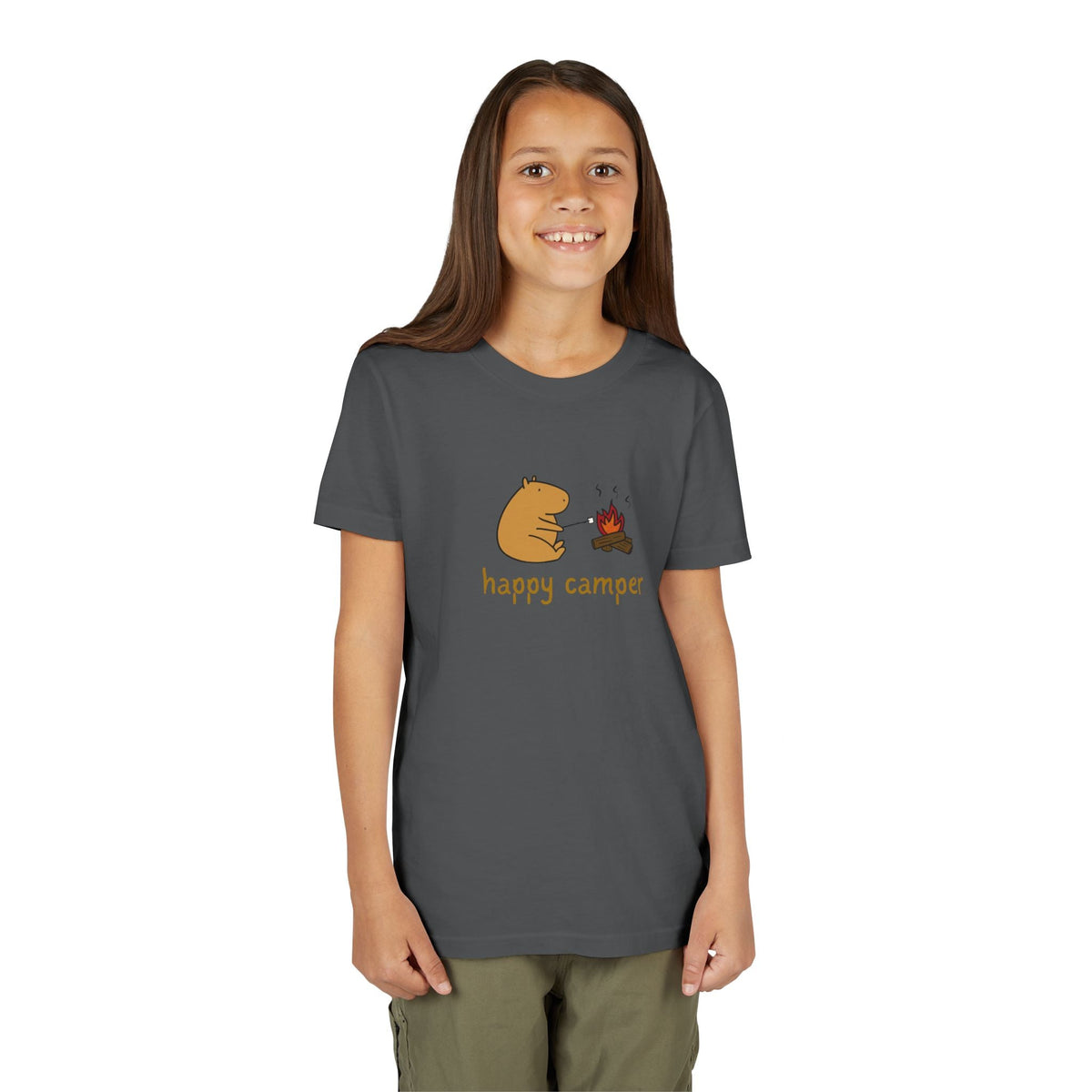 A young girl wearing a dark grey Capy Life t-shirt featuring a cute capybara roasting a marshmallow by a campfire.