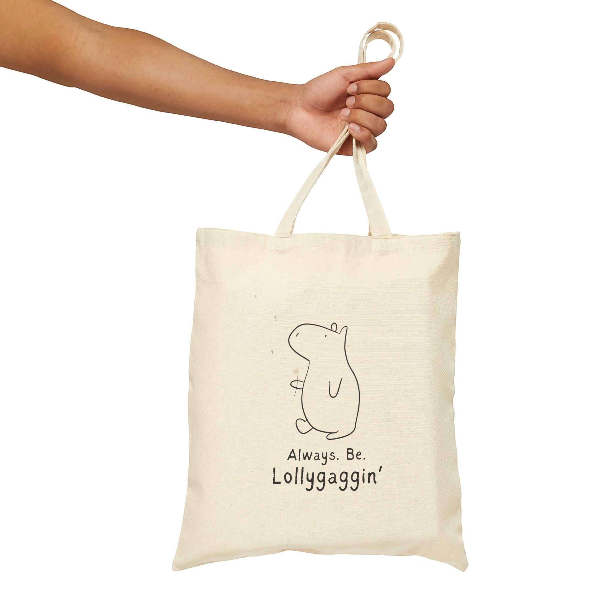 Capy Life natural canvas tote bag with a minimalist capybara illustration and Always Be Lollygaggin text held by hand