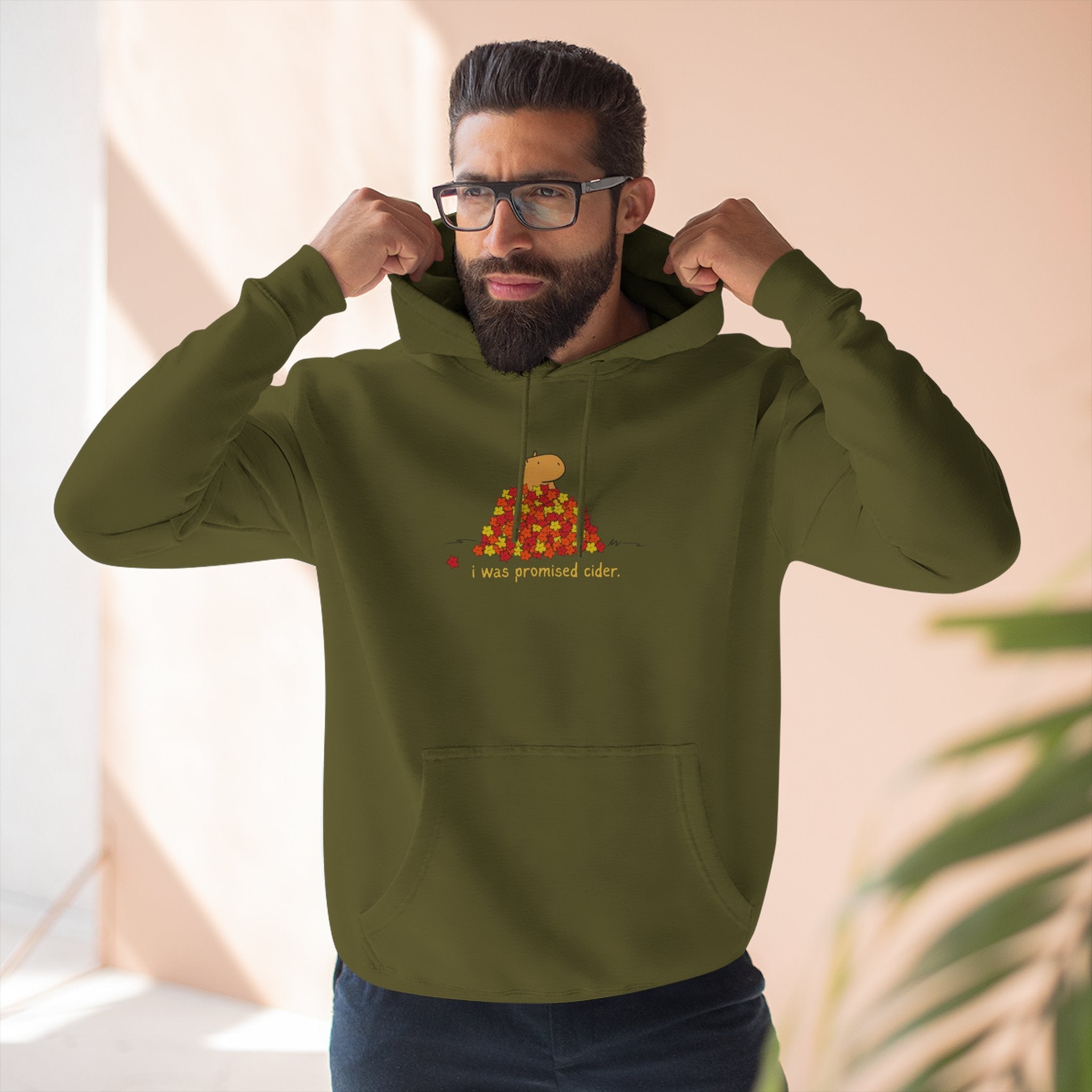 Man wearing a Capy Life olive green fleece hoodie with a funny capybara and autumn leaves graphic and text.