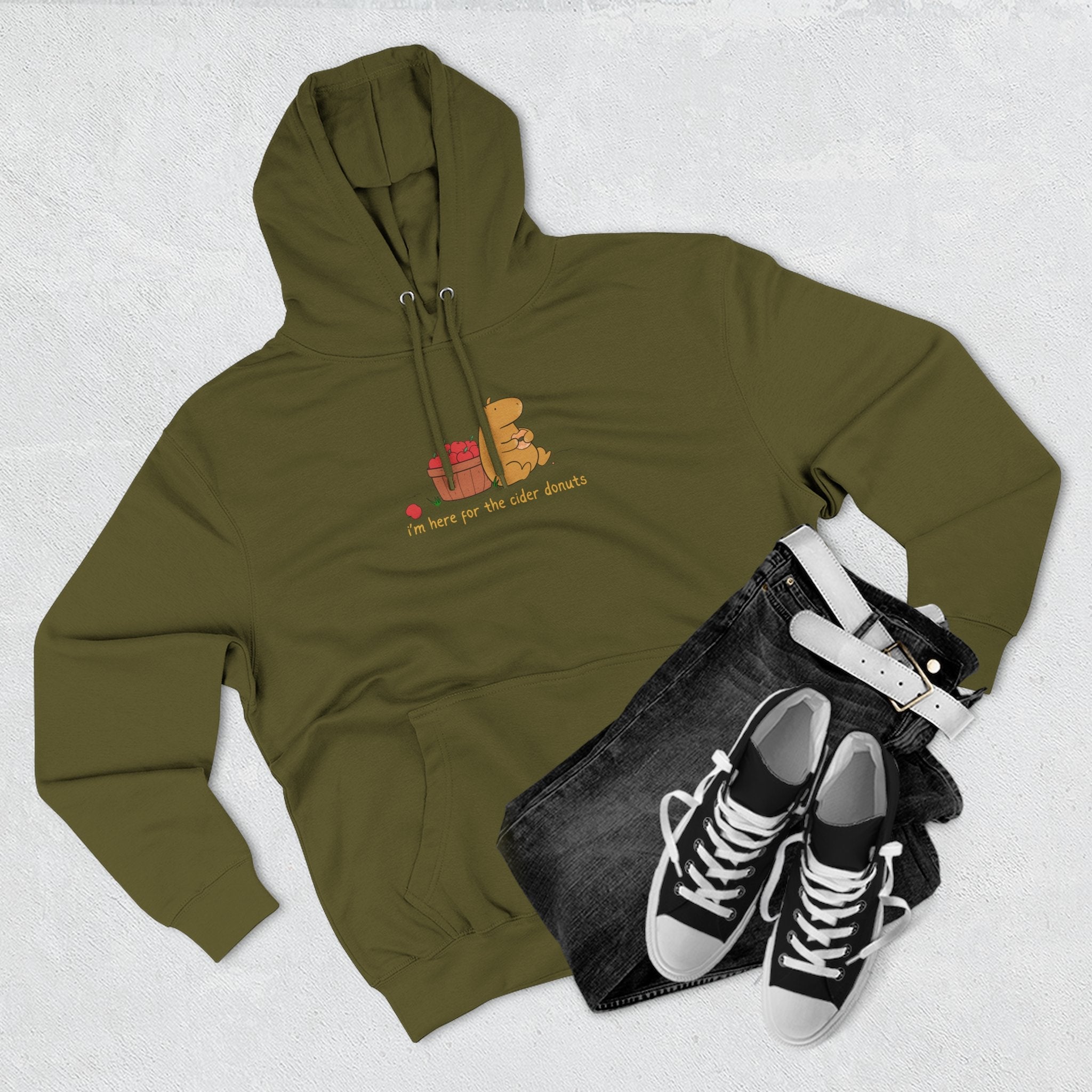 Capy Life olive green fleece hoodie with a cute capybara illustration and cider donut text, styled with black jeans.