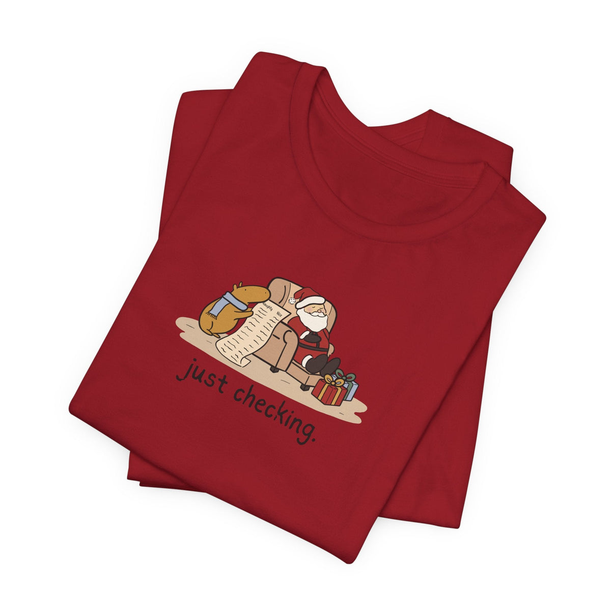 Capy Life red t-shirt featuring a hand-drawn capybara checking Santa's naughty or nice list while he naps.