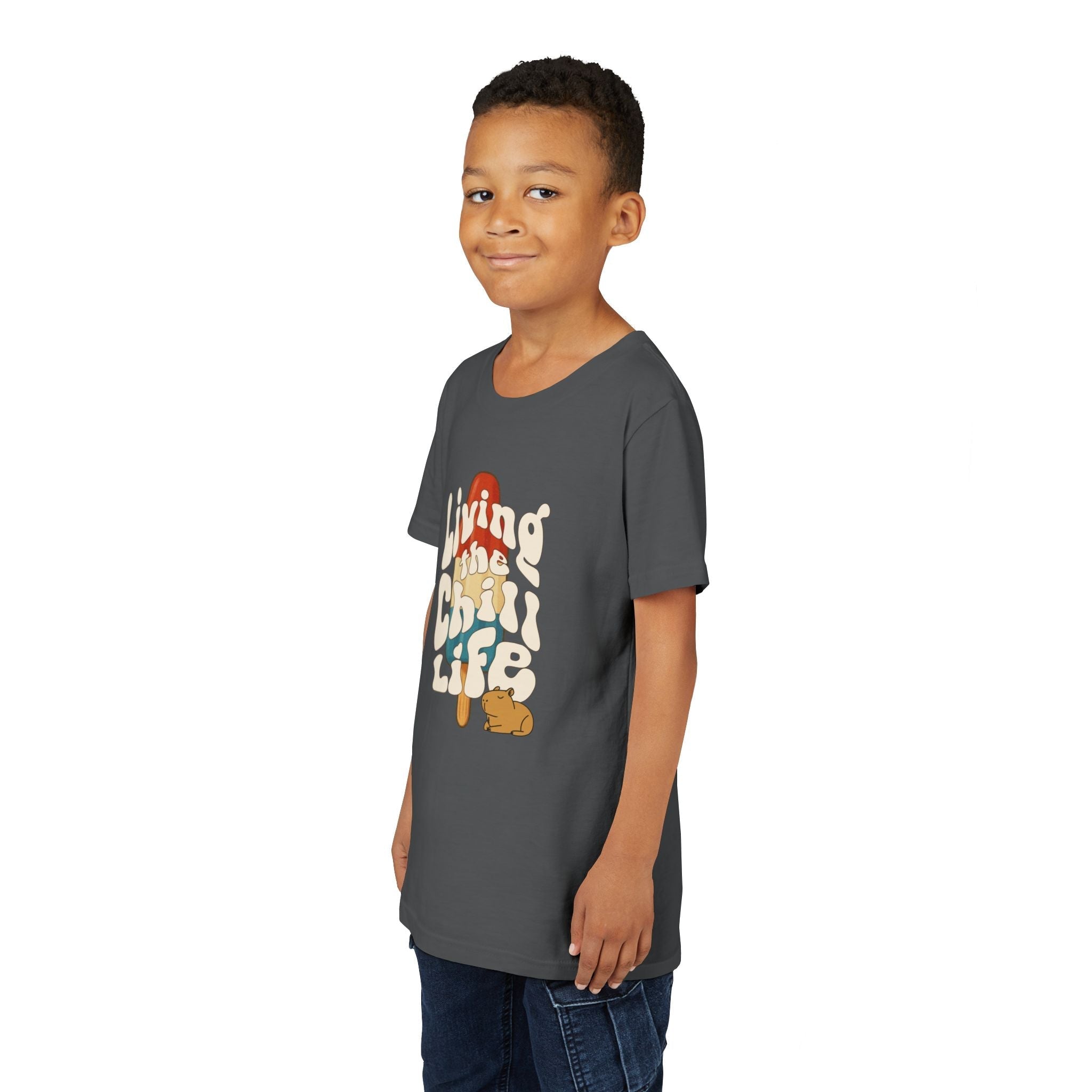 A young boy wearing a dark grey Capy Life youth t-shirt with a retro popsicle and capybara graphic design.