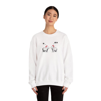 Person wearing a white crewneck sweatshirt featuring a graphic of two capybaras wearing red Santa hats facing each other with 'HO HO HO' text above them