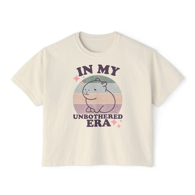 Cream-colored boxy women's t-shirt with text "IN MY UNBOTHERED ERA" and a cute capybara graphic in pastel colors