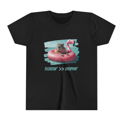 Unisex youth t-shirt with a capybara floating on a pink flamingo-shaped inflatable in an ocean setting with text "Floatin' >> Drippin'".
