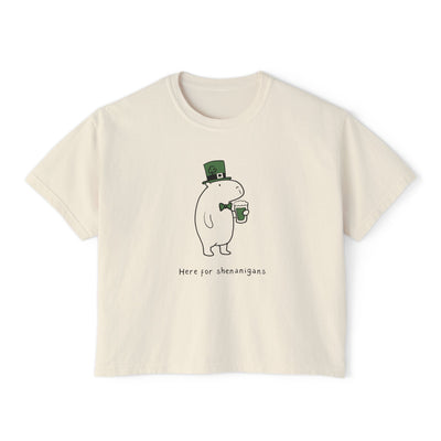 Cream-colored women's boxy t-shirt with a cartoon character holding a green beer mug and wearing a leprechaun hat, text "Here for shenanigans".