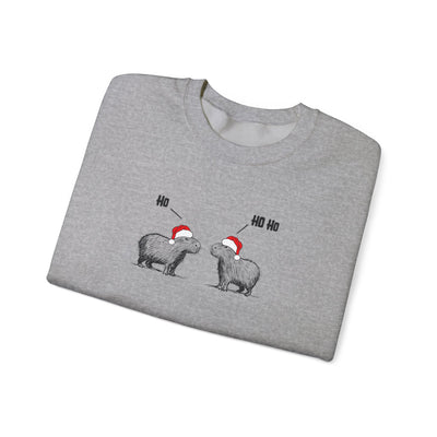 Folded gray crewneck sweatshirt featuring a graphic of two capybaras wearing red Santa hats facing each other with 'HO HO HO' text above them