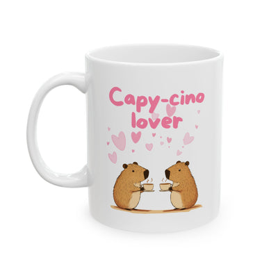 A white ceramic mug with the text "Capy-cino lover" and two cartoon capybaras holding coffee cups, surrounded by pink hearts.