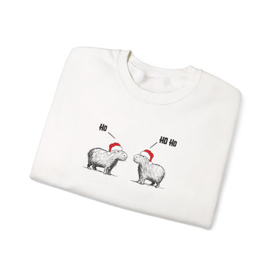 A folded white crewneck sweatshirt featuring a graphic of two capybara animals wearing red Santa hats, with one labeled 'Ho' and the other 'Ho Ho', on a plain white background.
