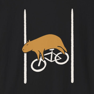 A black short-sleeve crewneck t-shirt featuring a graphic of a brown capybara riding a white bicycle between two vertical white lines on the chest, displayed against a solid white background.