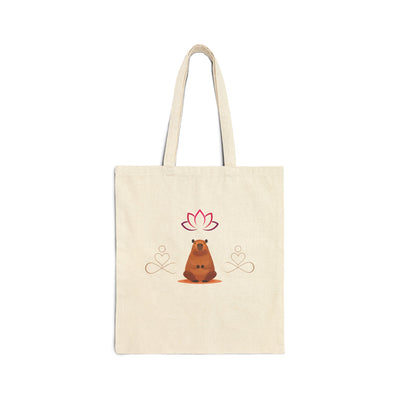 Cream-colored canvas tote bag featuring a cartoon bear in a meditative pose with a lotus flower above and heart symbols around.