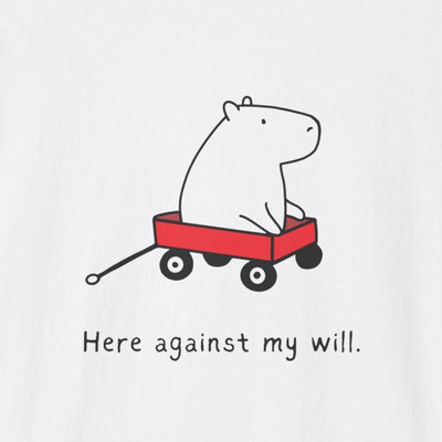 A white short-sleeve crewneck t-shirt featuring a cartoon graphic of a white capybara pulling a red wagon with the text 'Here against my will.' printed below it.
