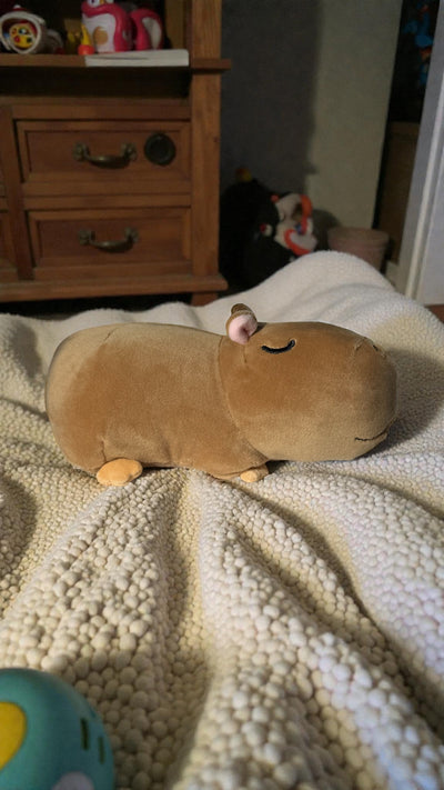Gene capybara plush on textured blanket in child's bedroom with stuffed animals