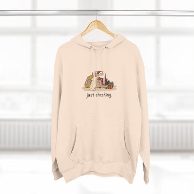 Capy Life beige fleece hoodie featuring a cute capybara checking Santa's naughty-or-nice list, with a kangaroo pocket.
