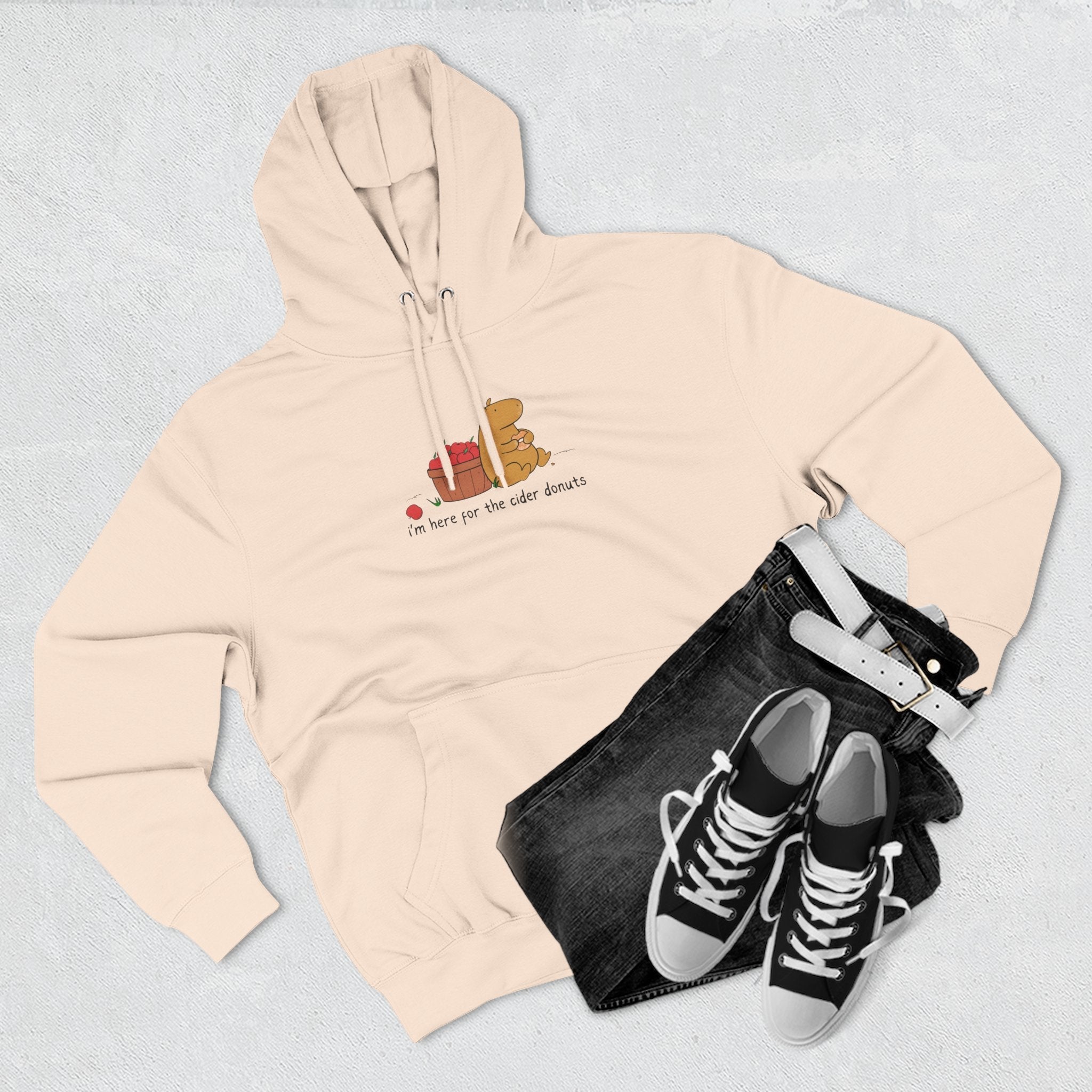 Capy Life beige fleece hoodie featuring a hand-drawn capybara eating a cider donut next to a basket of red apples
