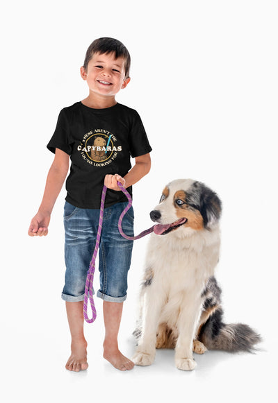 Capy Life youth black t-shirt featuring a Jedi capybara comic badge design, worn by a smiling boy with his dog.