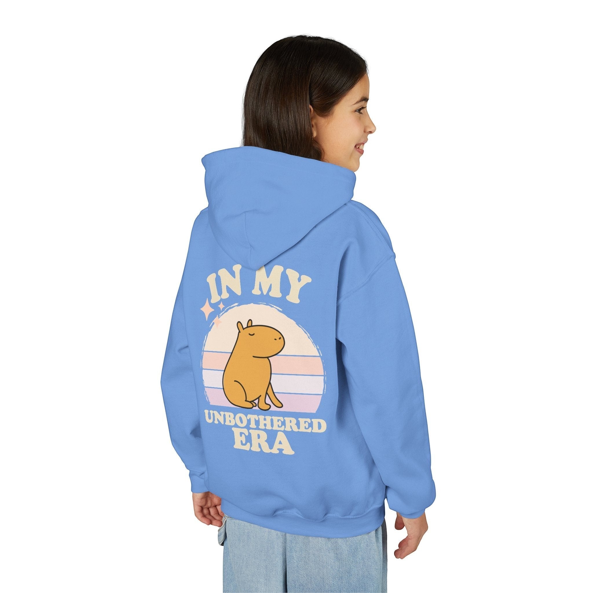 A girl wearing a blue Capy Life hoodie with a retro sunset and capybara graphic on the back with In My Unbothered Era text.