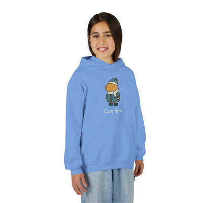 A young girl wearing a light blue Capy Life Cozy-bara hoodie featuring a cute capybara graphic in winter gear.