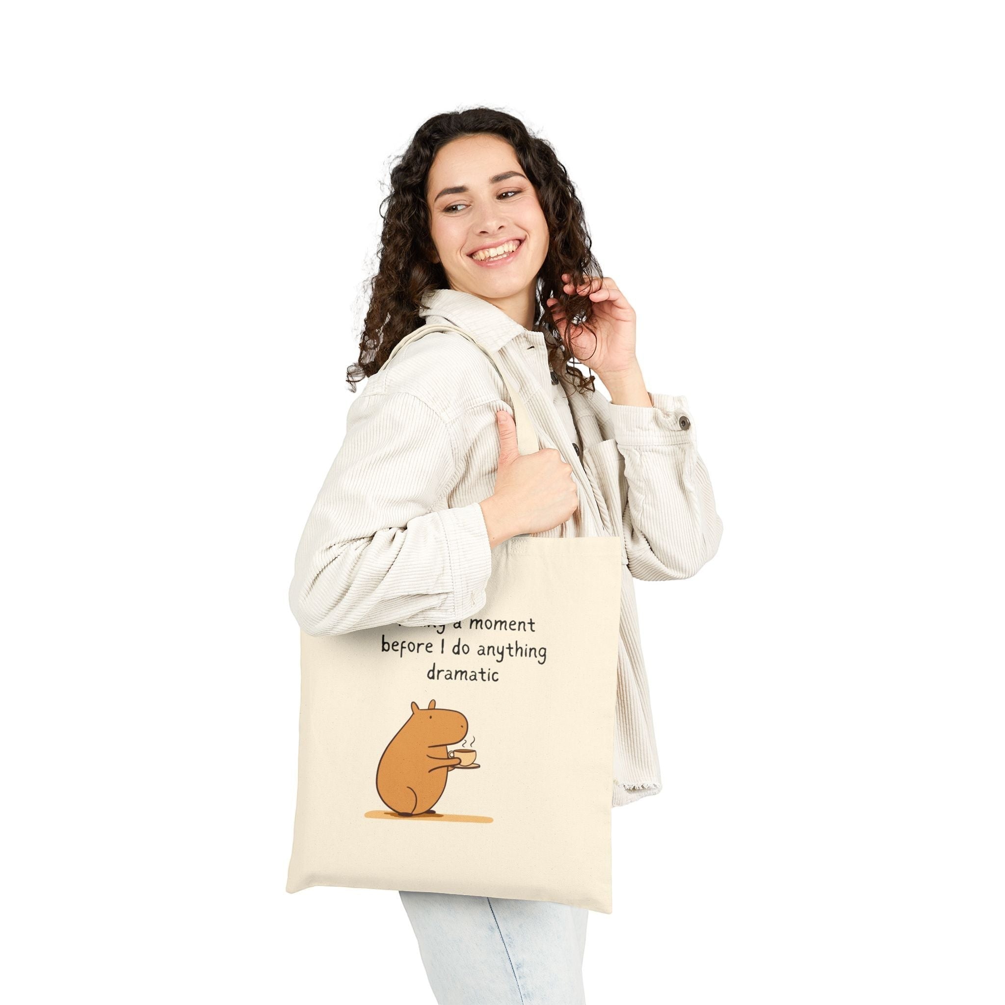 A woman carrying a natural Capy Life canvas tote bag featuring a capybara drinking coffee and a humorous quote.