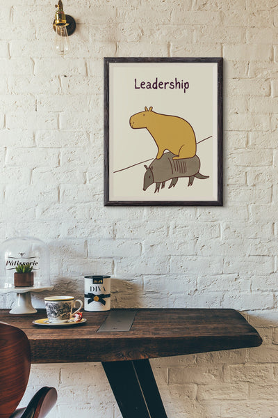 Capy Life minimalist wall art print featuring a capybara riding an armadillo, displayed in a frame on a white brick wall.