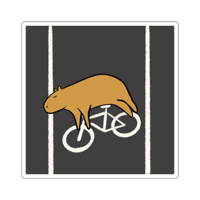 Capy Life vinyl sticker featuring a relaxed brown capybara lying across a white bike lane symbol on a charcoal background