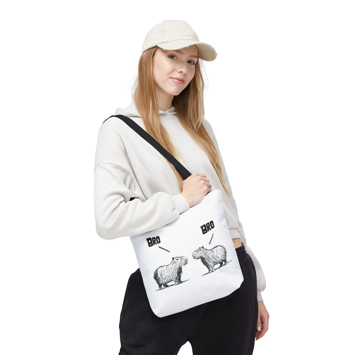 Capy Life premium white canvas tote bag with funny capybara line art, worn by a woman in a beige hoodie and cap.