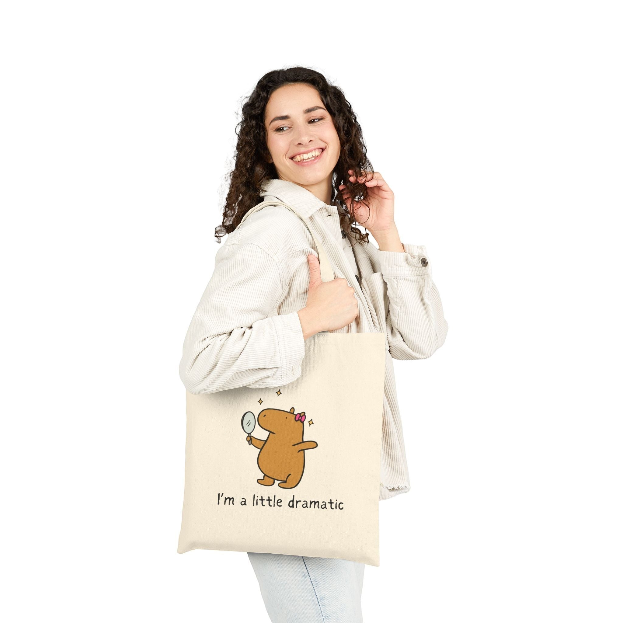 A woman wearing a Capy Life natural cotton canvas tote bag featuring a cute capybara graphic with a mirror.