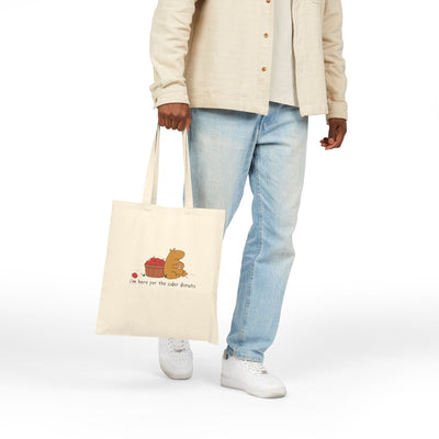 Capy Life natural canvas tote bag featuring a cute capybara with apples and a cider donut held by a person