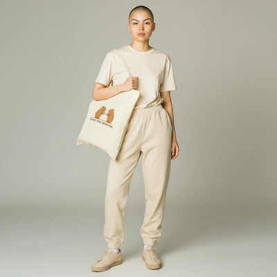 A model wearing a beige outfit carries a Capy Life canvas tote bag featuring a hand-drawn capybara coffee illustration.