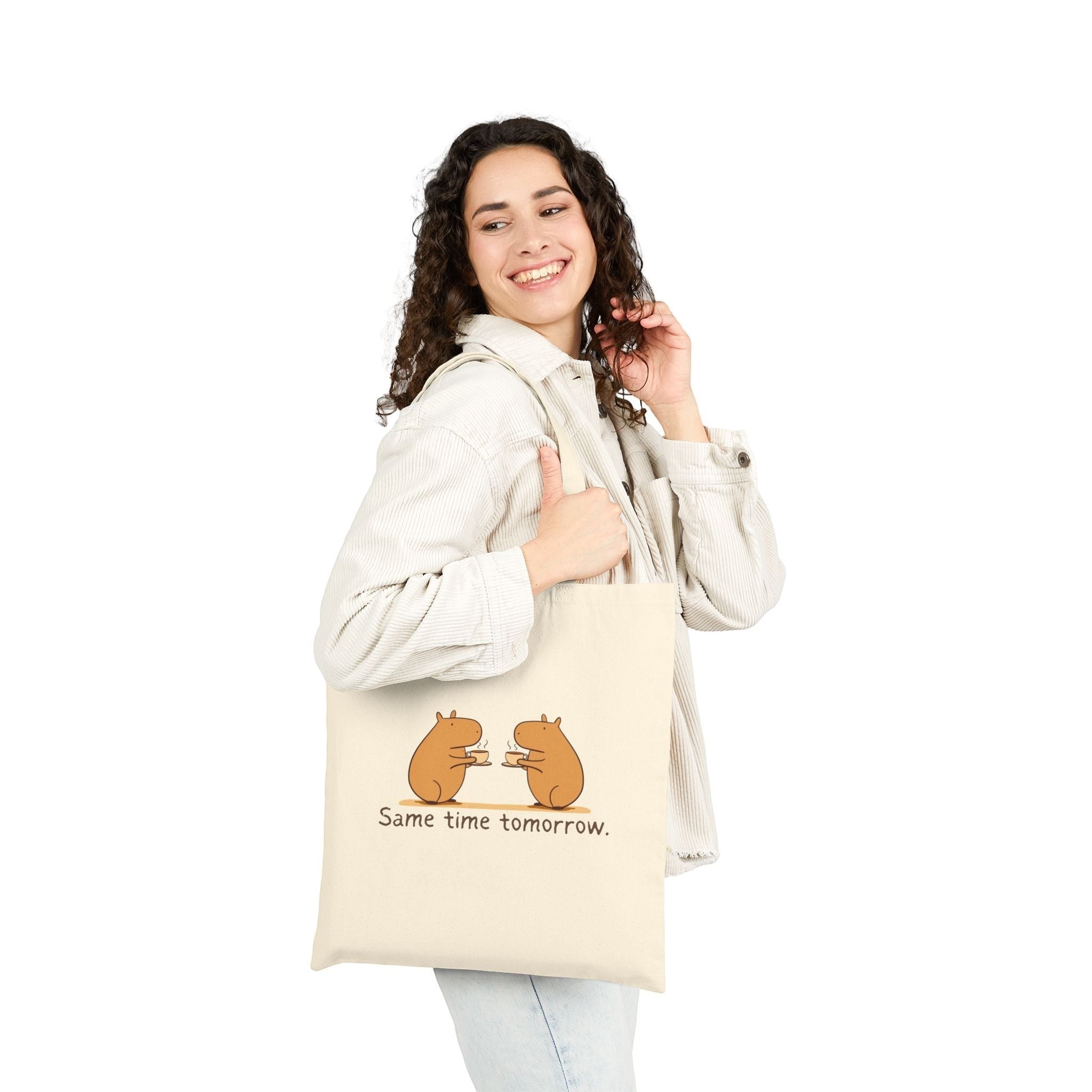 A woman wearing a corduroy jacket carries a Capy Life natural canvas tote with a capybara coffee illustration.