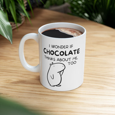 Capy Life white ceramic mug featuring a hand-drawn capybara illustration and the text I wonder if chocolate thinks about me, too on a wooden table.
