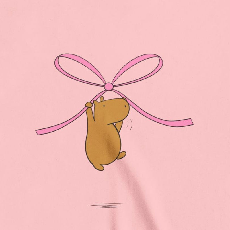 Capy Life kids t-shirt featuring a cute brown capybara hanging from a large pink coquette ribbon bow on pink fabric