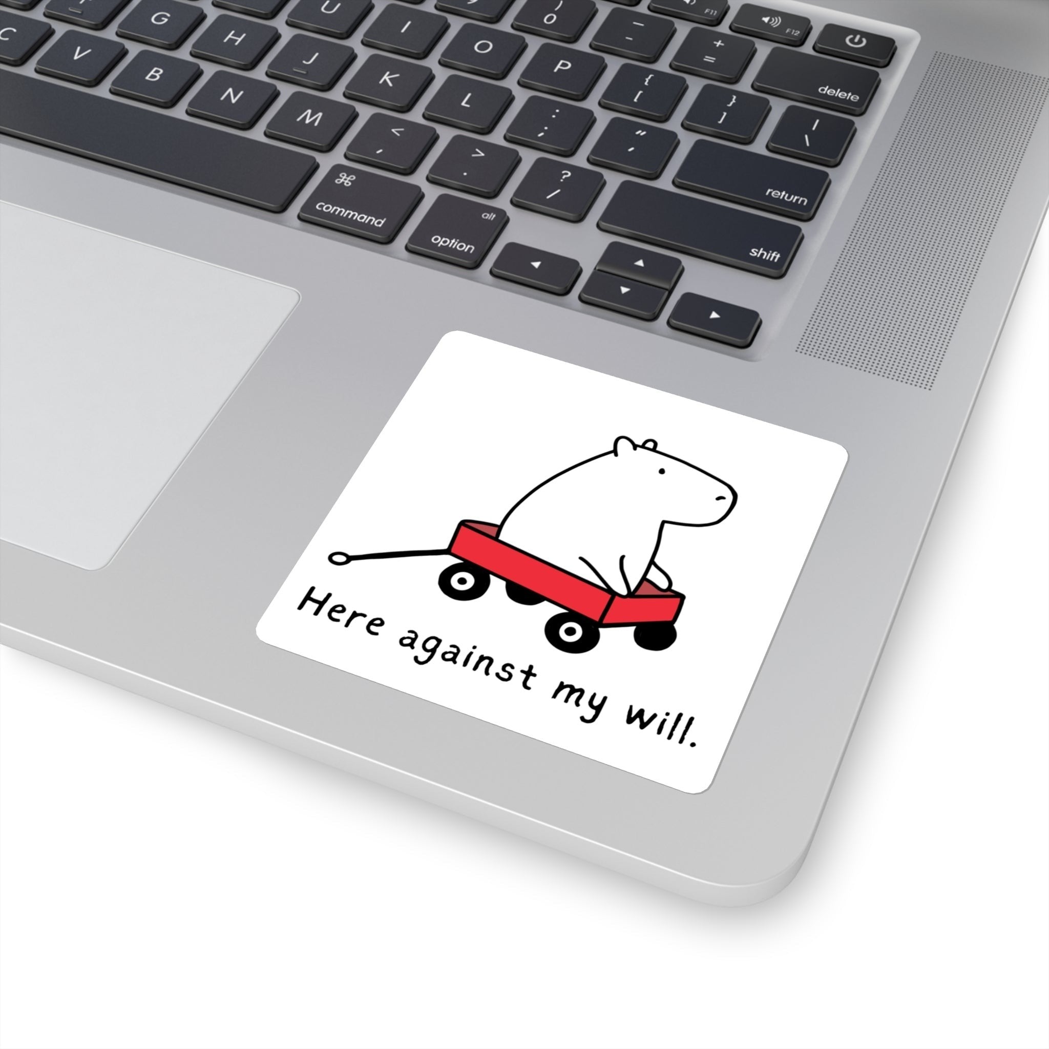 Capy Life vinyl sticker featuring a capybara in a red wagon with the text Here against my will on a laptop