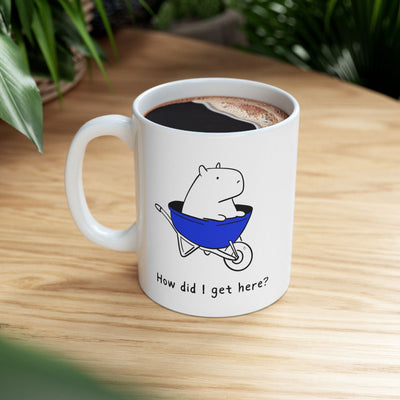 Capy Life white ceramic coffee mug featuring a cute capybara sitting in a blue wheelbarrow with the text How did I get here?