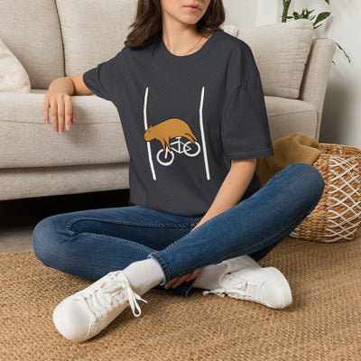 Woman wearing a dark grey Capy Life softstyle t-shirt with a funny graphic of a tired capybara on a bicycle.