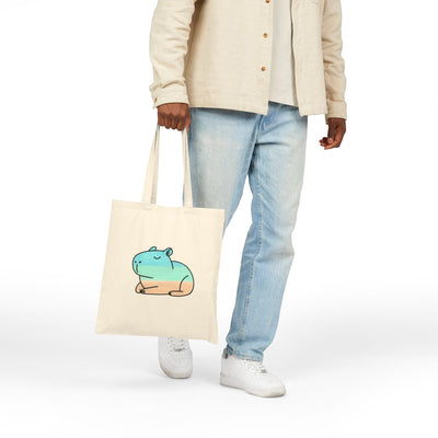 Capy Life coastal capybara canvas tote bag with hand-painted style illustration held by a person in casual clothing.