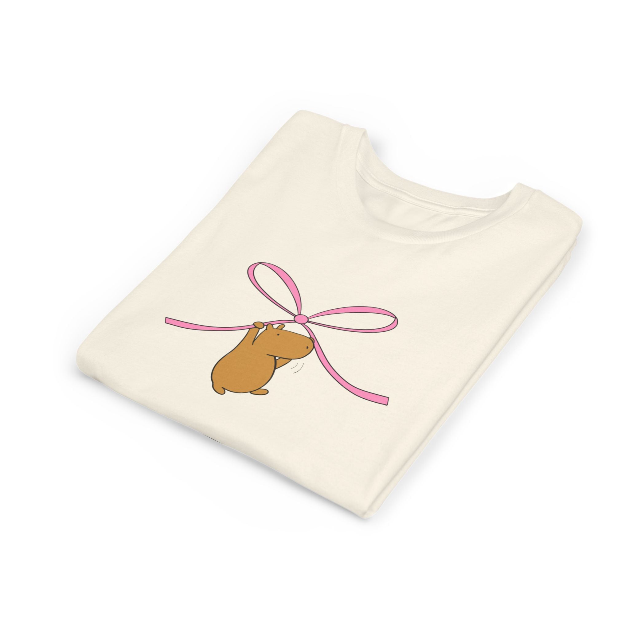 Capy Life kids t-shirt in cream cotton featuring a cute brown capybara hanging from a pink coquette ribbon bow
