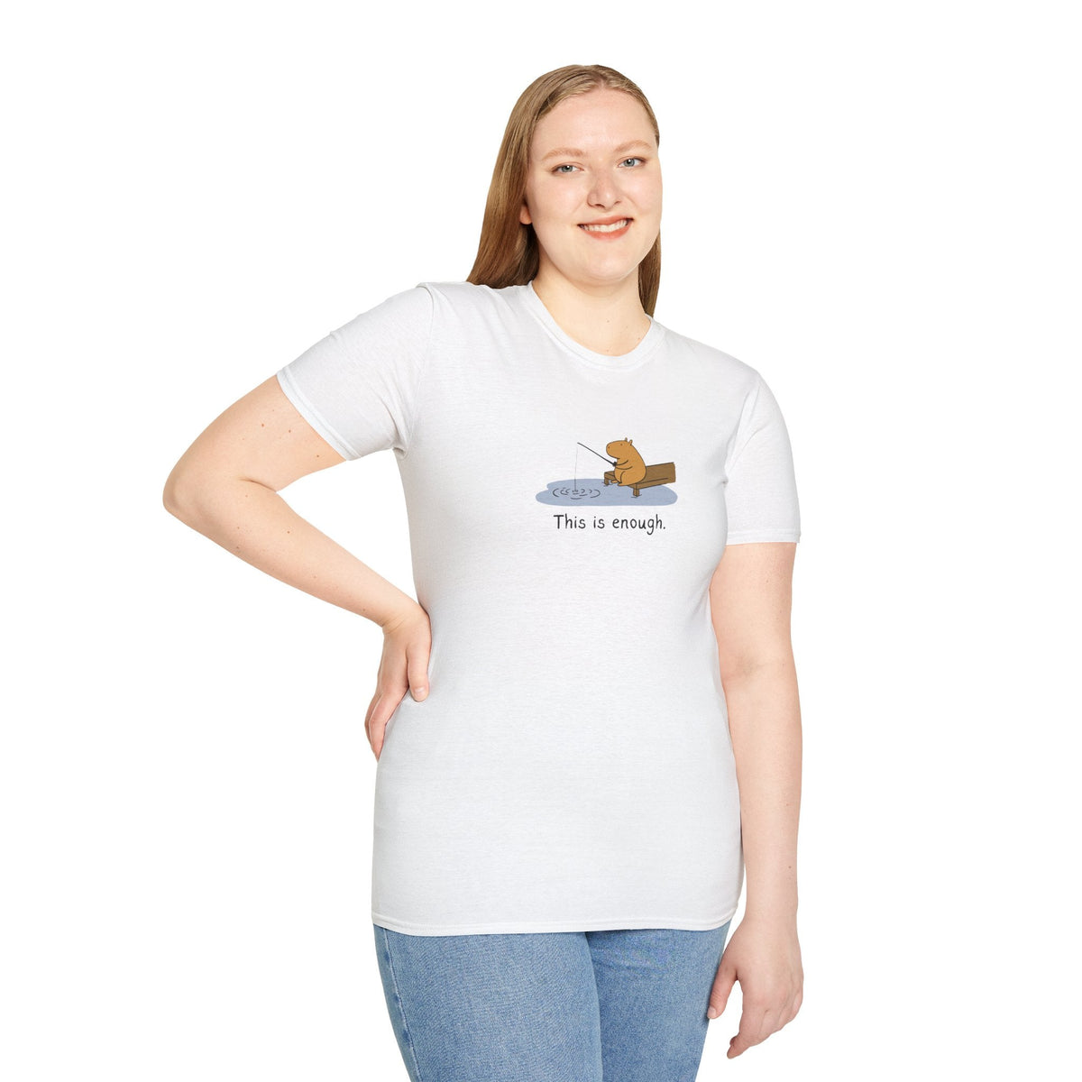 A woman wearing a white Capy Life softstyle t-shirt featuring a hand-drawn capybara fishing with the text This is enough.