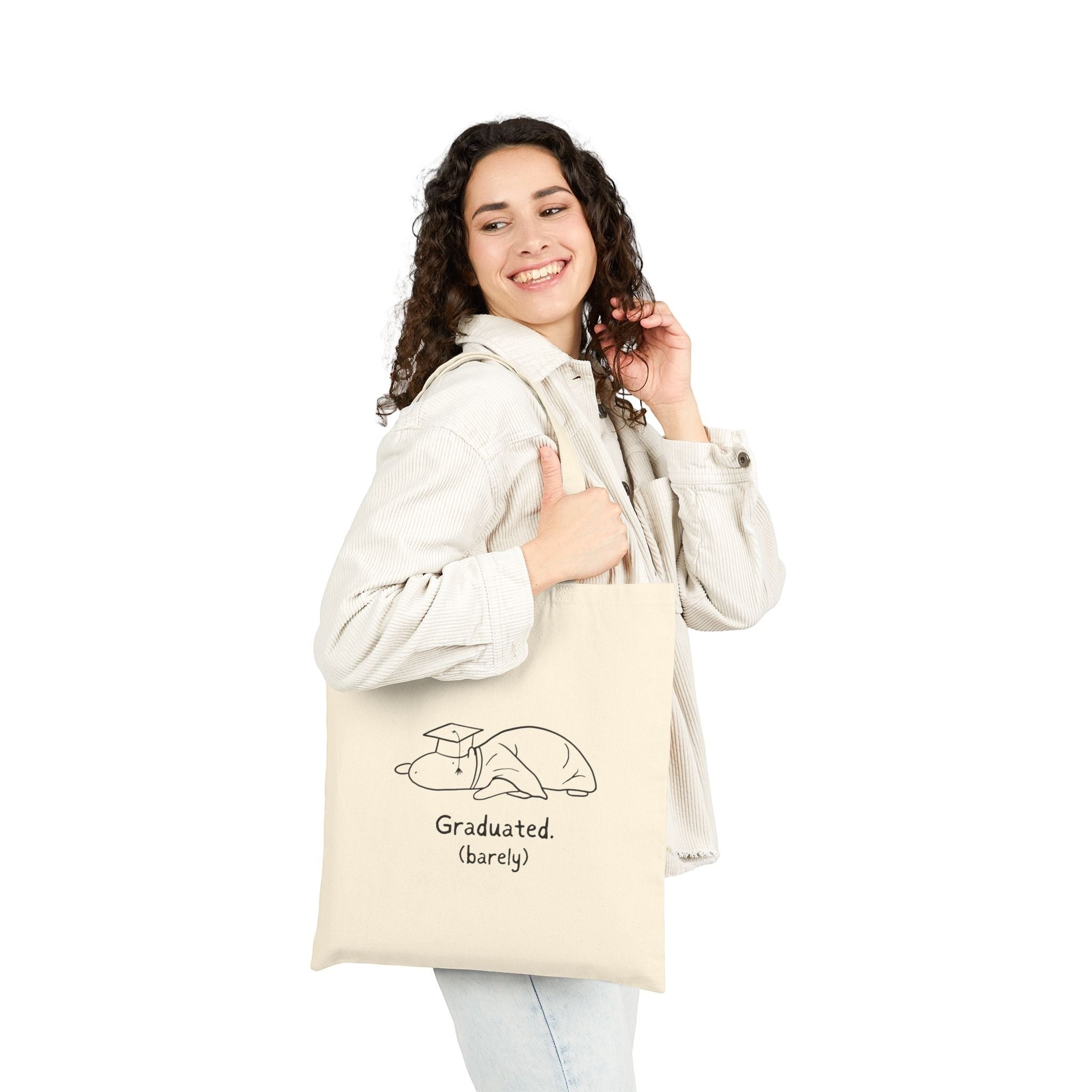 A woman wearing a Capy Life natural cotton canvas tote bag with a funny capybara wearing a graduation cap illustration.