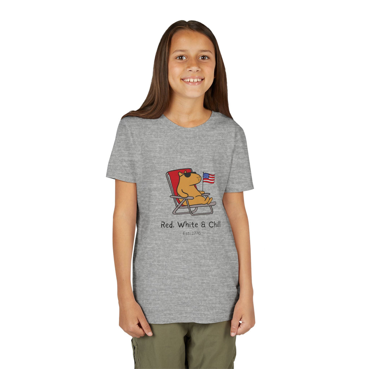 A young girl wearing a Capy Life heather grey youth t-shirt featuring a capybara lounging with an American flag.
