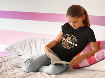 Capy Life youth t-shirt featuring a Jedi capybara comic badge design, worn by a girl reading on a bed.